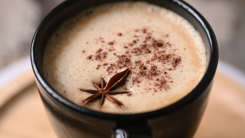 Chai Latte in Black Mug with Spices( star anise and cinnamon) on wooden table