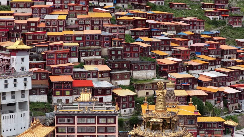 Aerial view of the Gatuo Monastery with dense clusters of red-walled buildings and golden roofs cascading down the hillside, Sichuan, China.
