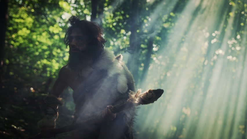 Portrait of Primeval Caveman Wearing Animal Skin and Fur Hunting with a Stone Tipped Spear in the Prehistoric Forest. Primitive Neanderthal Hunter Ready to Throw Spear in the Jungle