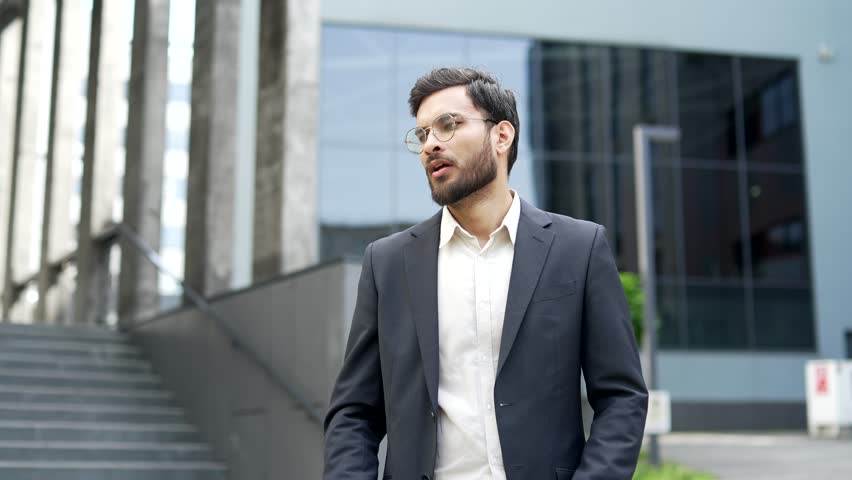 Unhealthy businessman in a formal suit coughing standing on street near office building. Sick man with a cold or flu feels bad, holds his hand to his chest. He has bronchitis, a virus or inflammation