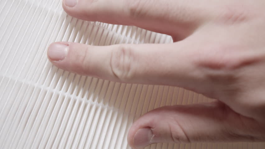 Human hand touches pleated air filter surface in close-up to examine material texture for quality inspection demo.
