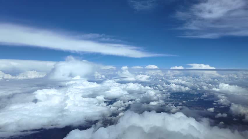 An immersive cockpit view through the pilot’s eyes while flying peacefully in a blue sky, over cottony storm clouds. Ultra-realistic 4K footage.