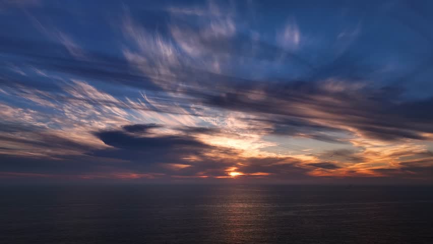 Aerial view of a striking sunset over the ocean, with vibrant orange and gold hues contrasting against the deep blue of the water, Los Angeles, California, United States.