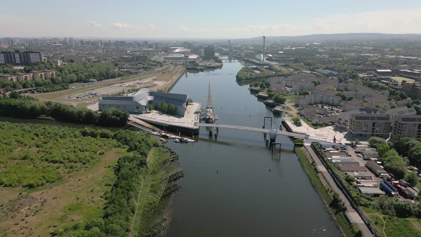 Aerial lower and tilt down over the River Clyde, Riverside Museum and Govan footbridge with Glasgow city skyline in distance, Glasgow, Scotland, UK