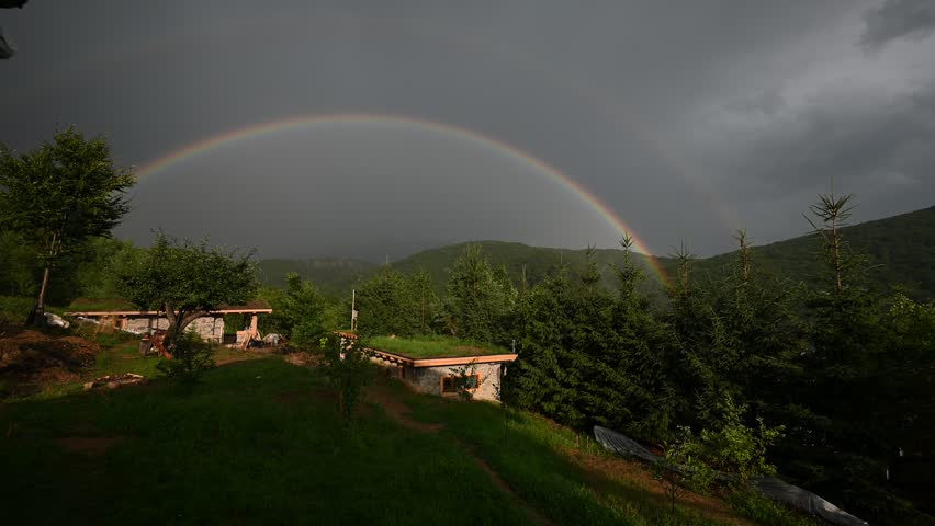 Beautiful Double Rainbow Arches Over a Mountain Landscape with Green Roofed Houses and Forest