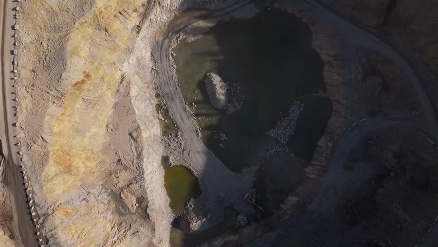 Aerial drone view of an active mine with conveyor belts moving crushed rock towards quarry stockpiles under bright sunlight