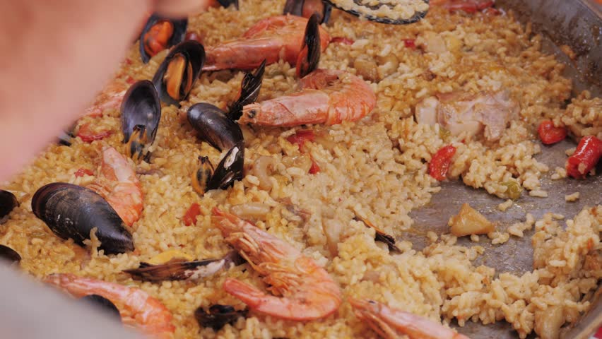 Chef Cooking traditional Spanish Paella on a stove, food festival in barcelona spain. Chef cooking food on fire from mussels, shrimp, squid rice, Catalan catalonian cuisine, street food truck.