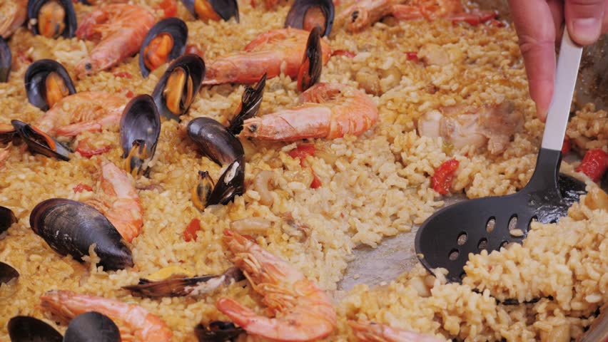 Chef Cooking traditional Spanish Paella on a stove, food festival in barcelona spain. Chef cooking food on fire from mussels, shrimp, squid rice, Catalan catalonian cuisine, street food truck.