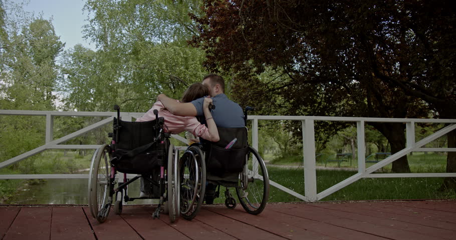 A loving and inclusive couple in wheelchairs shares a tender hug on a scenic park bridge. Capturing moments of support, commitment, and serene outdoor connection.