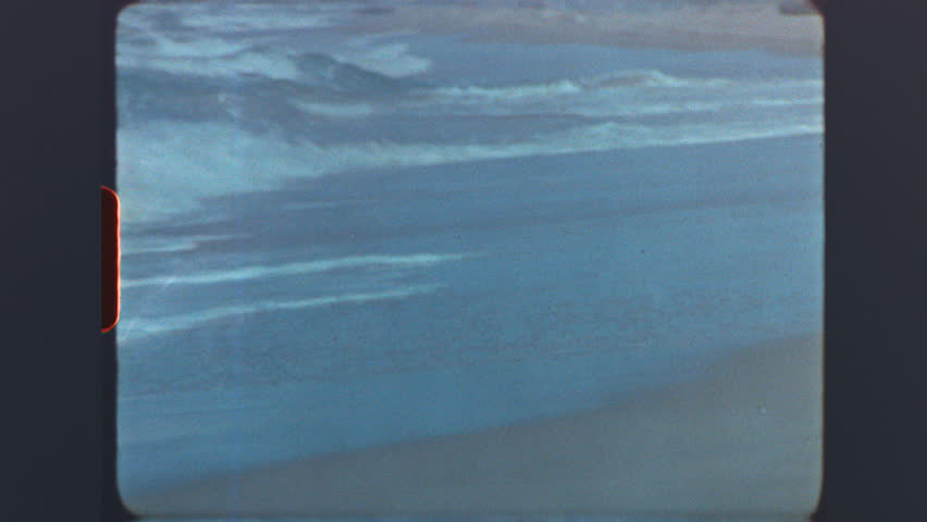Ocean waves rolling onto sandy shore captured on retro super 8mm vintage film