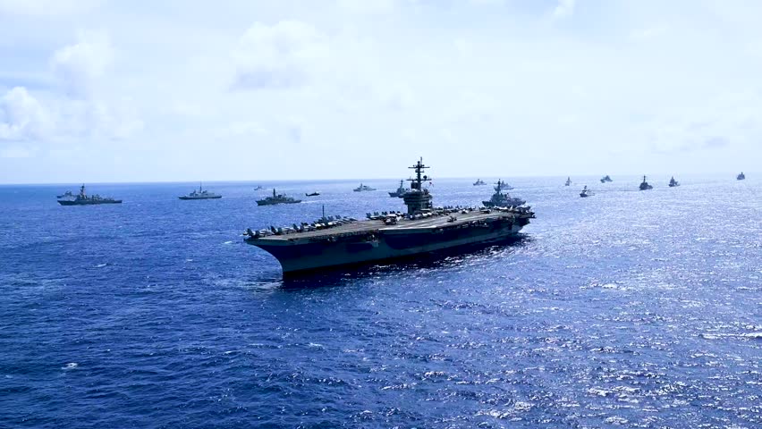An aircraft carrier and several other destroyer warships are seen sailing together.