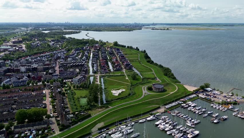 Muiden, North Holland, Netherlands - 09.06.2025 Aerial view of a marina with numerous sailboats and yachts docked, a channel leading into a wide lake or sea, and lush green landscape partly cloudy sky