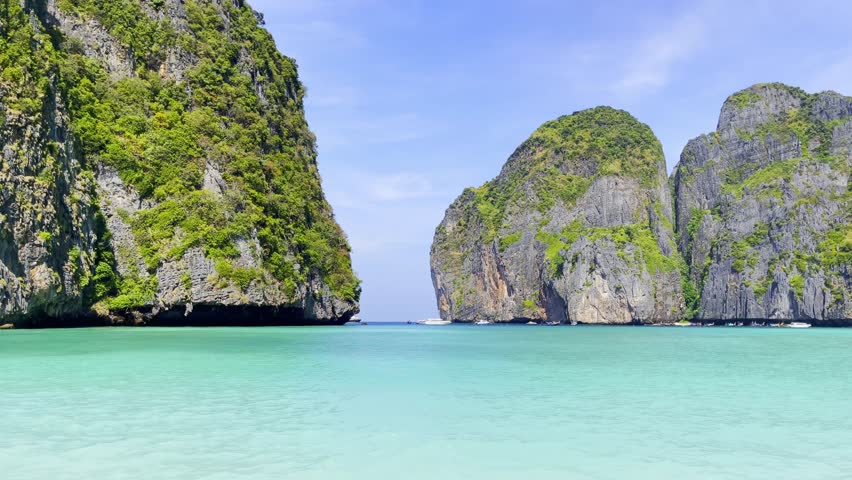Scenic view of Maya Bay in Koh Phi Phi islands, Thailand with turquoise water, towering limestone cliffs, and boats in the distance under a clear blue sky