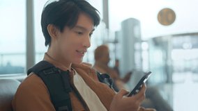 Happy young Asian man using smartphone while waiting for departure at airport terminal, checking flight details, browsing internet and social media before travel journey - Powered by Shutterstock - Get 15% off with code: PIKWIZARD15