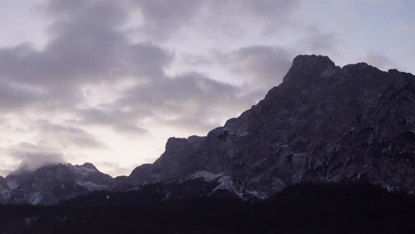 A shot of the Alps at dawn with clouds and a purple sky in Italy.