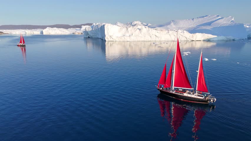 Little red sailboat cruising among floating icebergs in Disko Bay glacier during midnight sun season of polar summer. Ilulissat, Greenland. Global warming and melting glaciers.