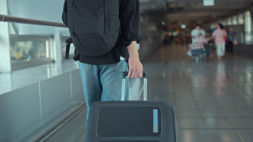Rear view - Male traveler walking with luggage or suitcase at the modern airport terminal, man on way to flight boarding gate, Ready for travel or vacation journey.