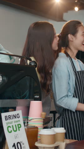 Vertical Screen : Portrait young Asia female barista happy with friend at urban cafe. Small business owner girl in apron taking selfies on mobile phone look to camera stand at counter in coffee shop.