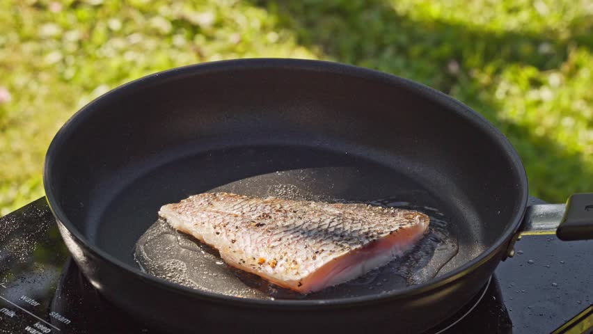 outdoor cooking. cook preparing fresh fish fillet on hot pan with oil for making delicious meal in garden, food closeup, outdoors natural light