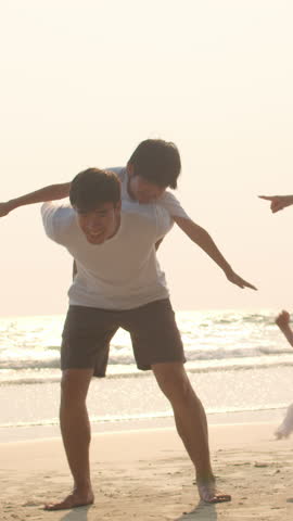 Vertical Screen : Asian young happy family enjoy vacation on beach in evening. Dad, mom and kid relax play together near sea when sunset. Lifestyle travel holiday vacation summer trip. Slow motion.