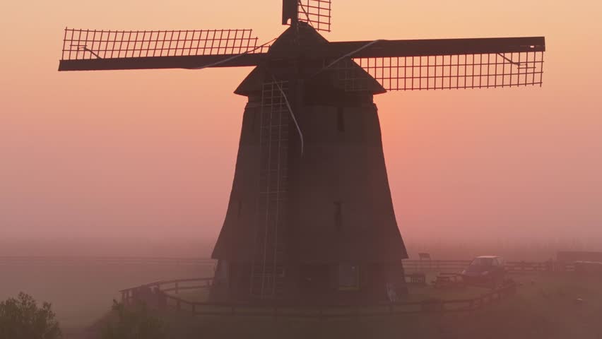 Aerial view of soft sunrise fog surrounding windmill and meadows, Netherlands