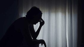 Silhouette of a woman sitting by a window, holding her head in distress, expressing anxiety, sadness, or emotional struggle. 4K with selective focus. - Powered by Shutterstock - Get 15% off with code: PIKWIZARD15