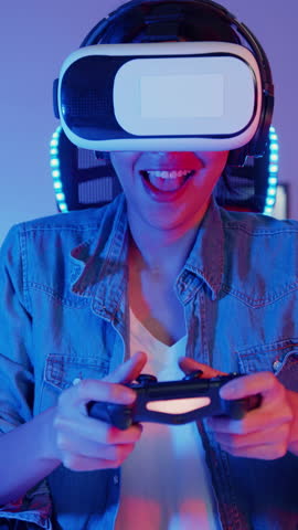 Vertical Screen : Happy young asia girl gamer winner wear virtual reality glasses goggles headset and joystick controller fun and excited with online game in neon home studio at night. Home activity.