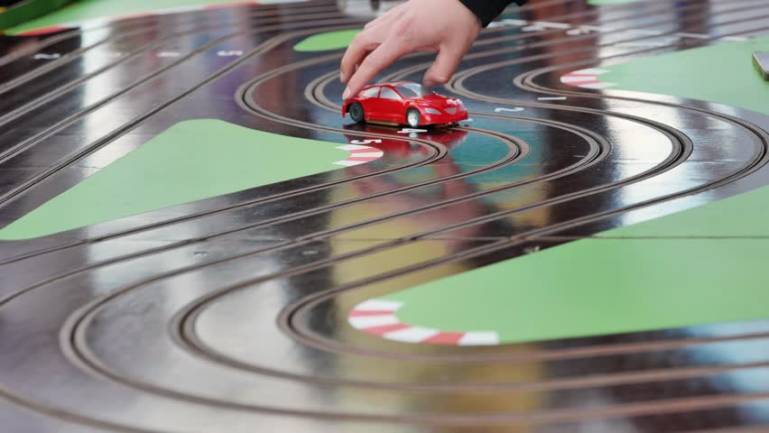 Hand pushing a red toy car on a slot car racing track during a sports day.