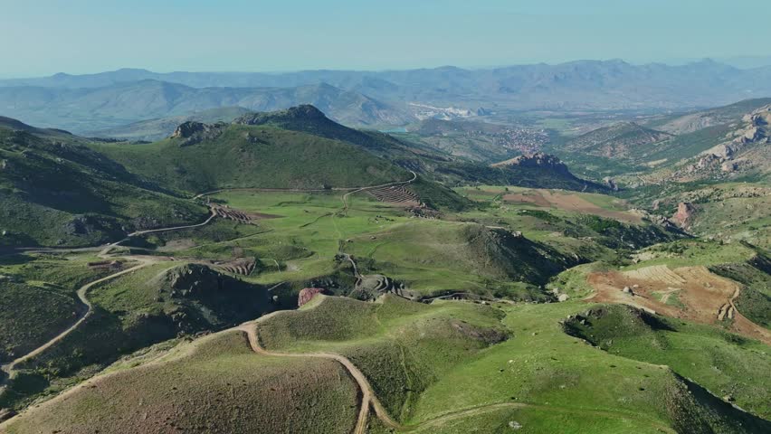 Aerial view of rolling green hills and mountains under a clear blue sky