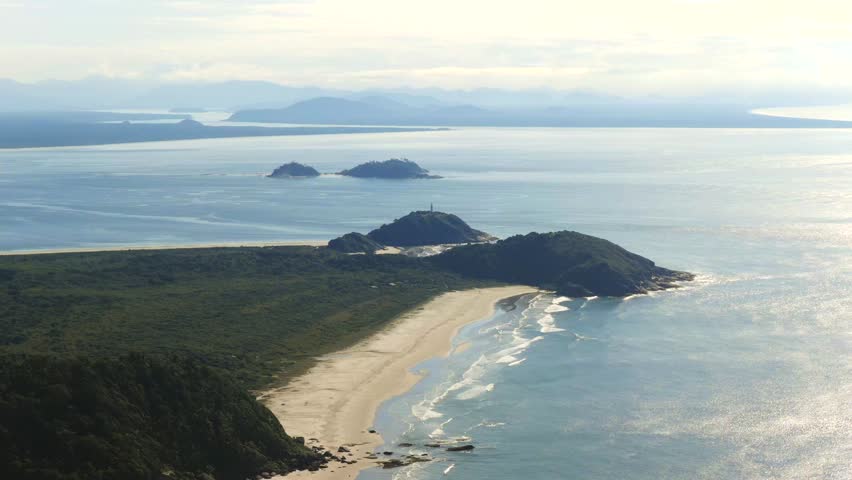 Aerial view of Ilha do Mel island long beach side stretching between forested hills and smaller islands, Paraná, Brazil.