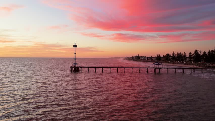 Wide aerial shot of Brighton Beach jetty at dusk with red colorful cloudy sunset, Adelaide, South Australia