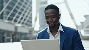 Portrait of positive African American employee with hearing impairment works on laptop in modern city. Businessman with disability processes commercial data on internet in downtown - Powered by Shutterstock - Get 15% off with code: PIKWIZARD15
