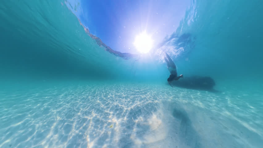 Young woman diving underwater. Slow motion video, woman in swimsuit swimming underwater in blue lagoon with sandy bottom. Vacation, freediver,  healthy lifestyle, travel