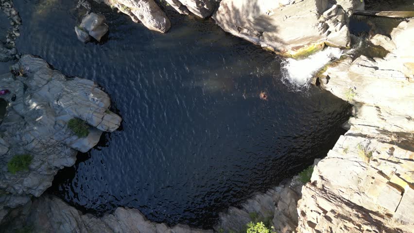 Aerial view of a natural pool surrounded by rugged rocks and sparse vegetation, a swimmer enjoys the cool waters, Catllar, Occitanie, France.