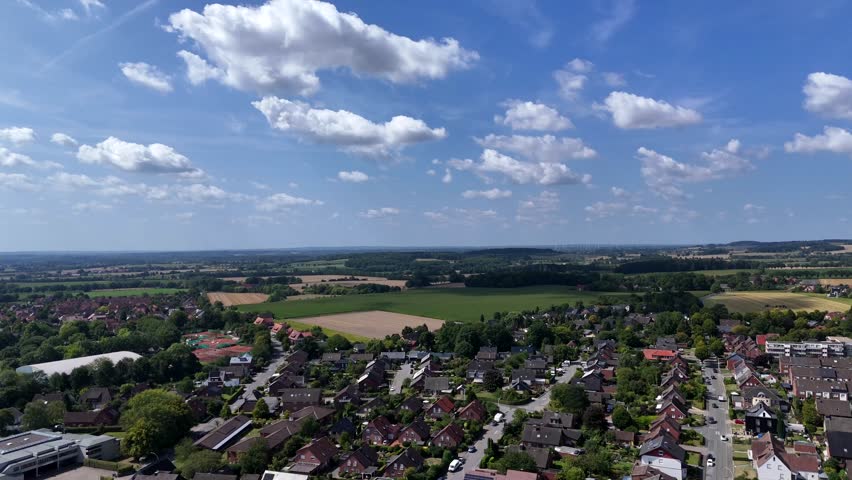 White clouds at blue sky over city in America. Neighborhood with brick houses and rural fields in distance. Wisconsin, United States. Peaceful landscape in nature. Aerial wide shot.