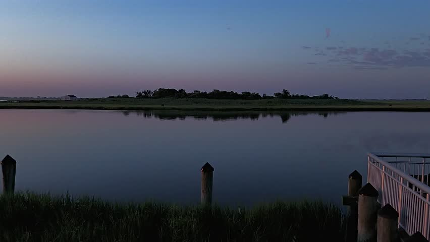 An aerial view of the salt marsh off Freeport, New York on a cloudy day. The drone camera dolly in and slowly boom up over the waters and green marsh grass.