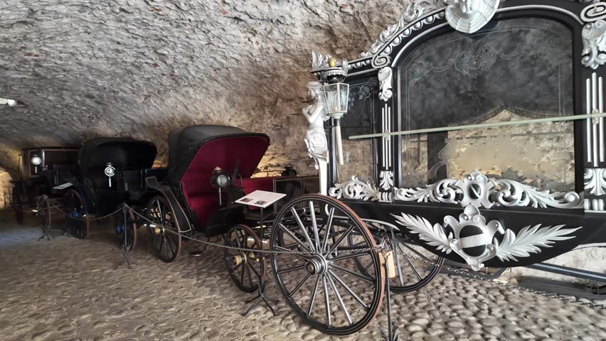 A silver-adorned medieval hearse rests in a castle tunnel. Angelic figures and lanterns shimmer against black embroidered cloth, evoking solemn beauty and timeless reverence.