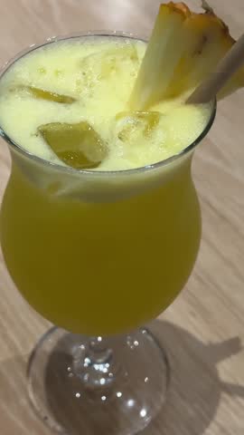 Tropical cocktail indoors Hand is mixing and decorating yellow pineapple ginger lemon smoothie with fresh mint. Vertical video. Healthy homemade blended drink.