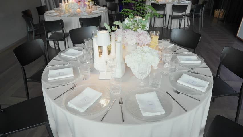 A white tablecloth-covered table set for group of people. It has an elegant centerpiece with white flowers and vases.