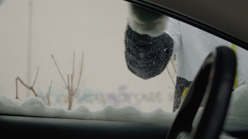 In freezing temperatures, a woman is determinedly removing snow from her car to prepare for travel. The challenging winter conditions highlight her effort and perseverance.