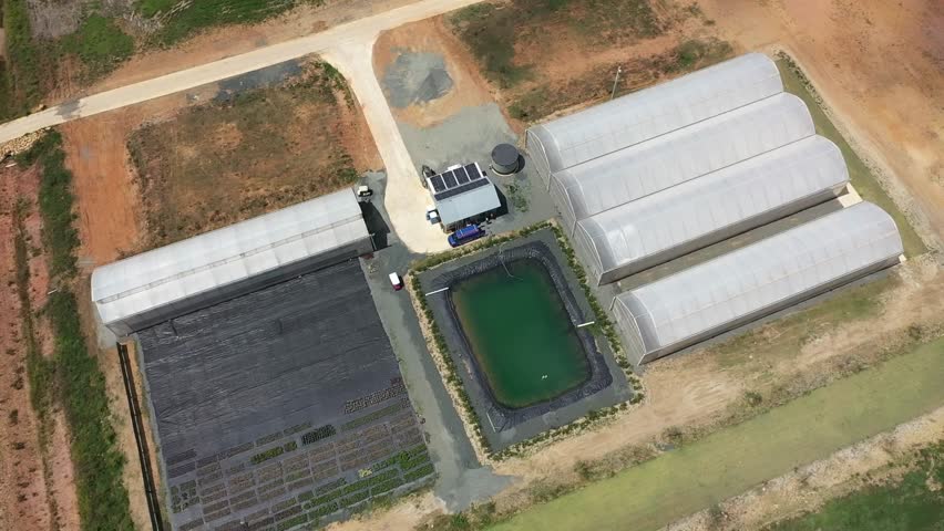 An Aerial top view of greenhouses with a central water pond and side planting plots with dirt paths