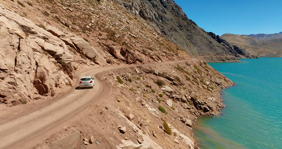 Aerial car driving along cliff edge of arid rocky canyon terrain and steep hills in Cajon del Maipo, Chile