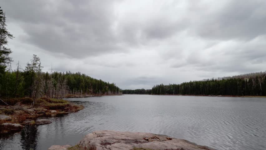 A time lapse of Caucasian man in northern Canadian wilderness, watching nature from a Granite Rocky point on a freshwater lake under clouds in Canada