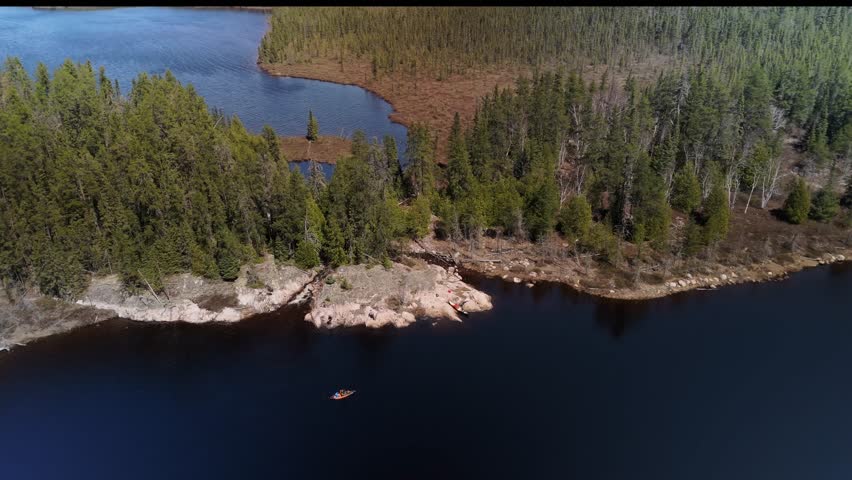 An aerial view of rocks and forest separating two freshwater lakes as a kayaker paddles along the granite shoreline in Timmins, Ontario, Canada