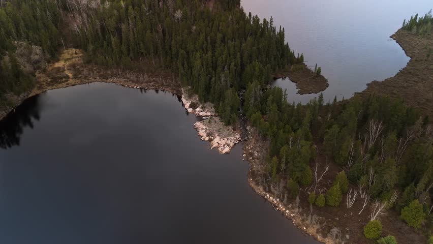 A slow zoom aerial view of granite stone and boreal evergreen forest separating two freshwater lake