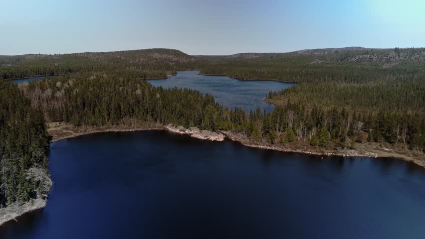 An aerial view of a serene lake surrounded by dense forest under a clear sky in Timmins, Ontario, Canada