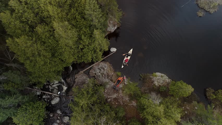 A drone shot of two men paddling a canoe from granite rocky shore of northern Ontario crown land revealing the vast evergreen forest landscape around