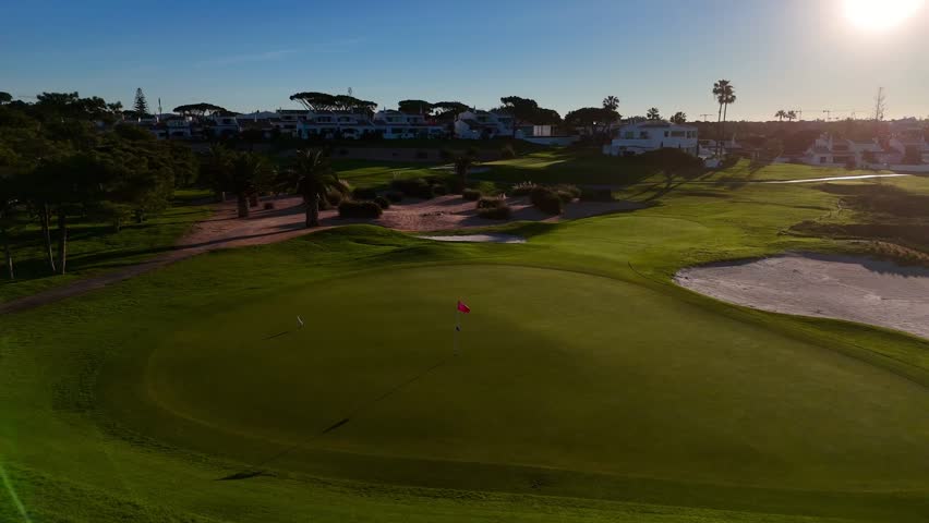 A Drone shot of a red flag in a green gold field  overlooking a calm ocean under clear blue skies