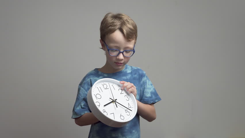 Little boy in glasses manually turns clock hands. White wall clock and school child. Back to school concept.
