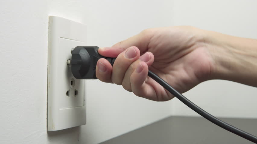 Female hand inserting a black electrical plug into outlet. Closeup view of a fork in a socket.